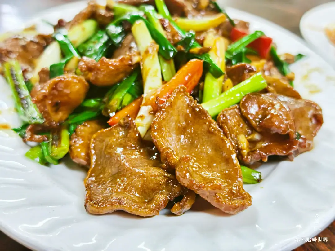 一盤爆炒牛舌近照，與翠綠的蔥段和橘色蔬菜一同拌炒，香氣四溢。