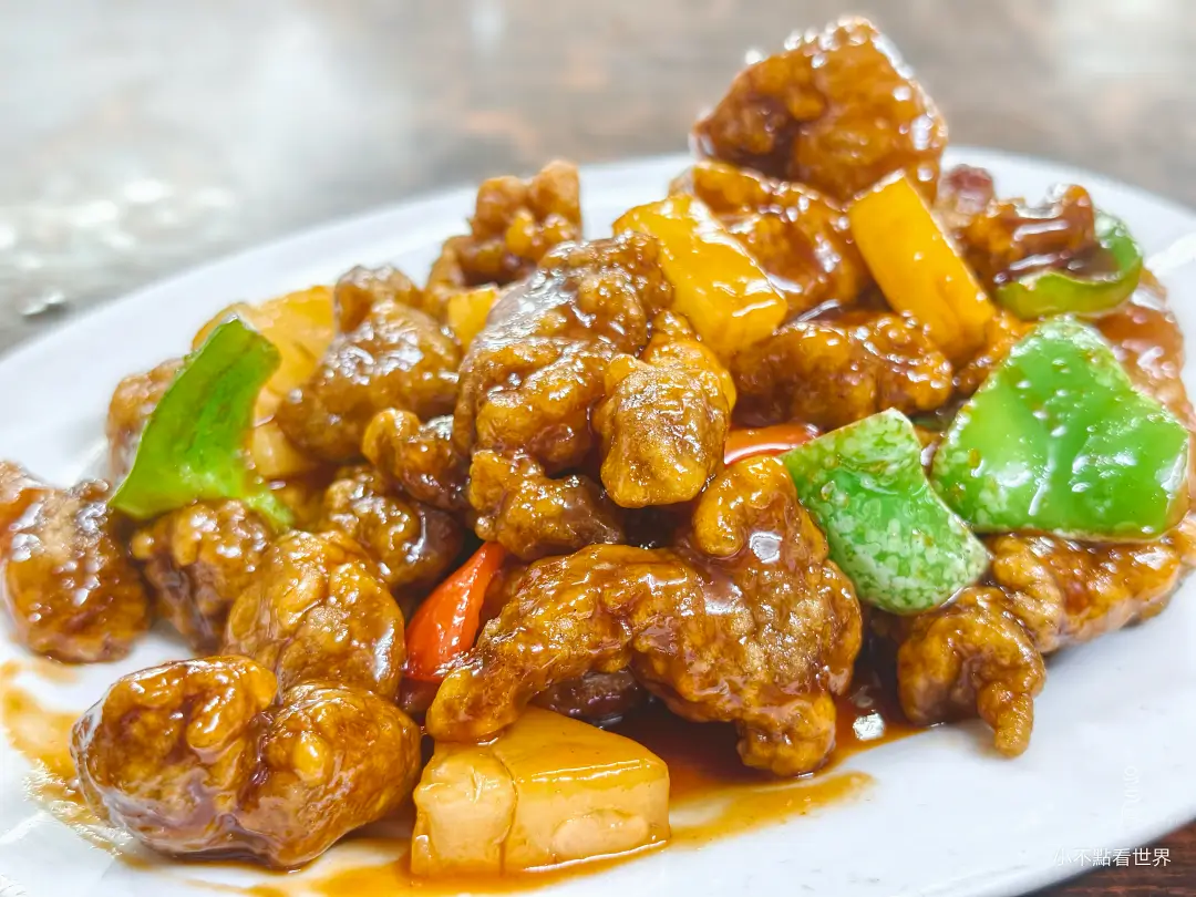 一盤色澤金黃的波羅咕嚕肉特寫，肉塊裹著濃郁醬汁，搭配切塊的鳳梨和青紅椒，呈現誘人光澤。